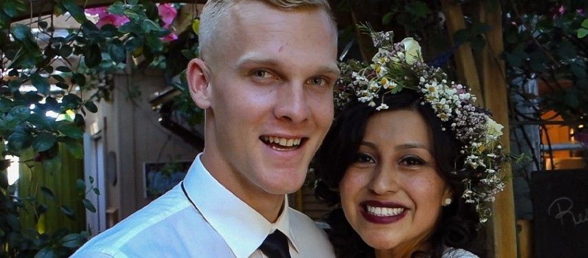 A man and a woman are posing for a picture . the woman is wearing a flower crown.