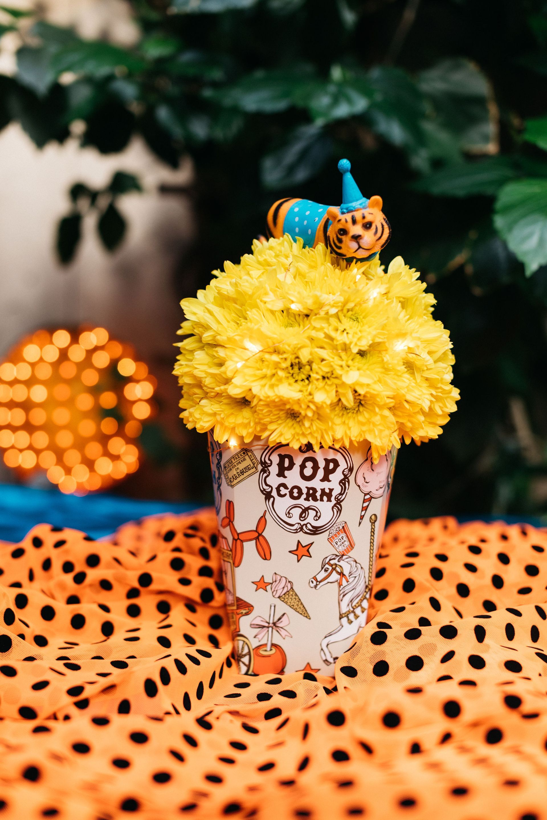 A popcorn bucket filled with yellow flowers and a tiger on top.