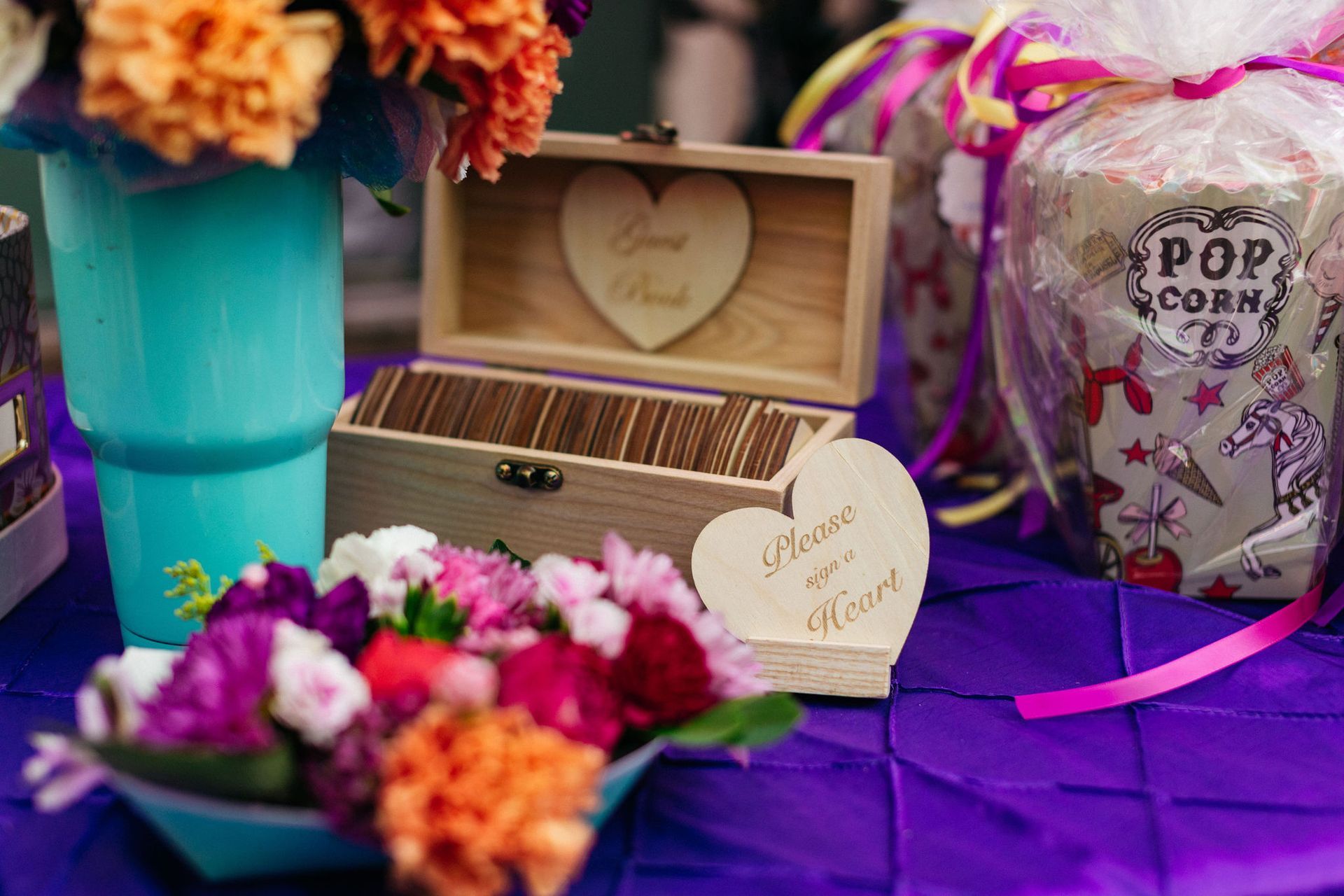 A wooden box with a heart on it is sitting on a table next to a vase of flowers.