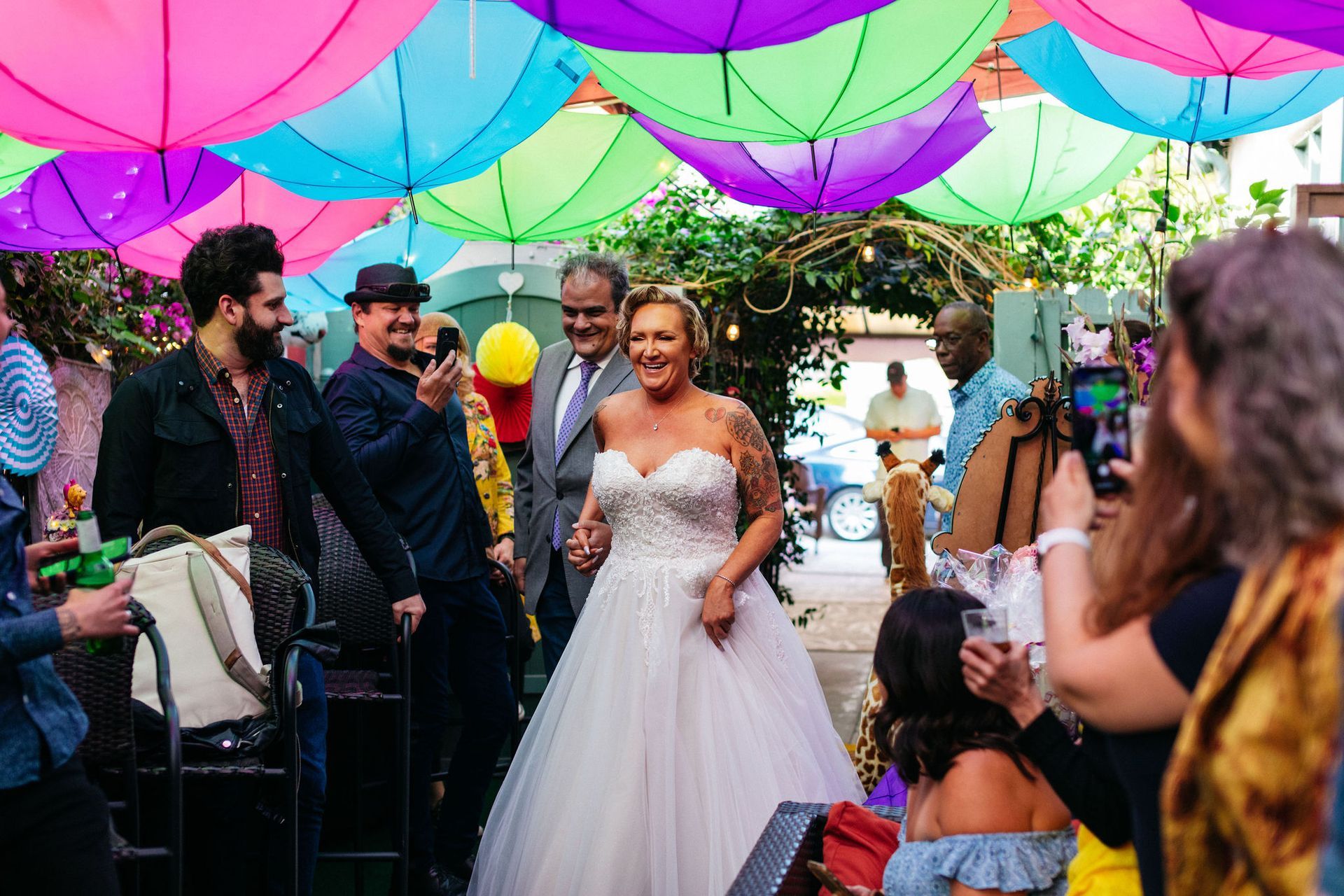 A bride and groom are walking down the aisle under colorful umbrellas.