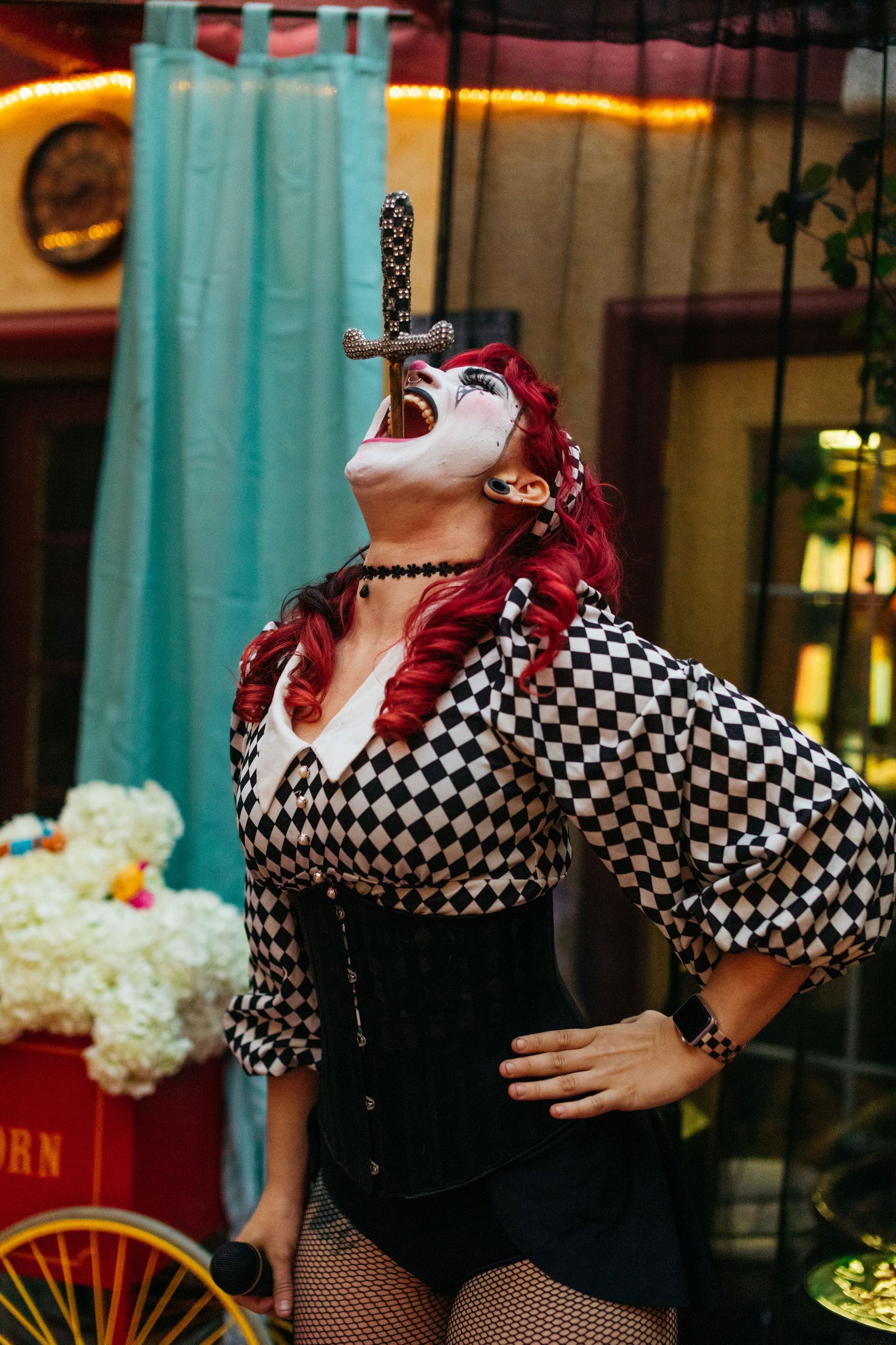 A woman in a clown costume is holding a snake in her mouth.