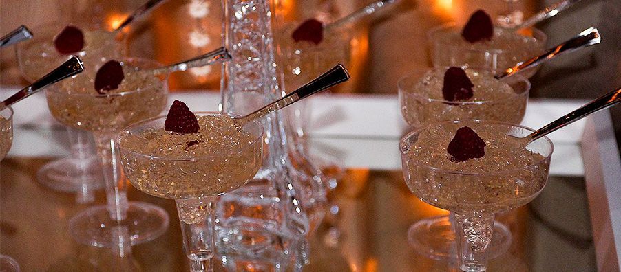 A row of champagne glasses filled with a dessert with raspberries on top.