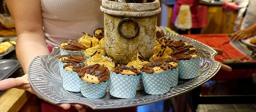 A woman is holding a tray of cupcakes with a candle on top of them.