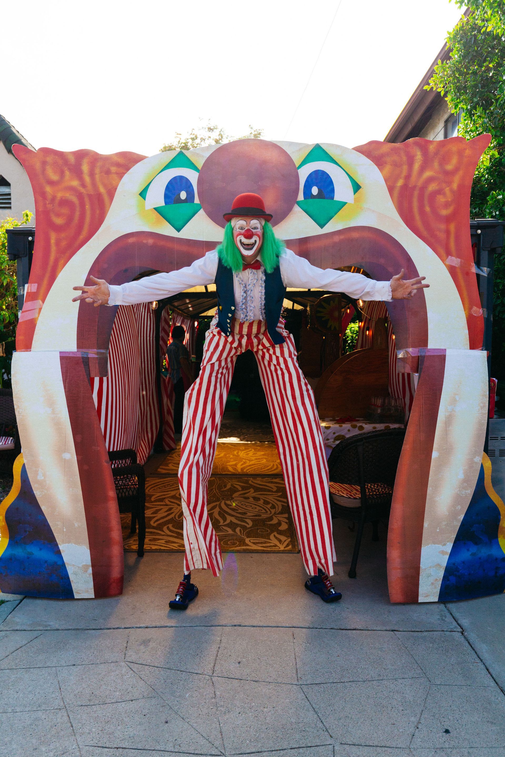 A clown on stilts is standing in front of a clown archway