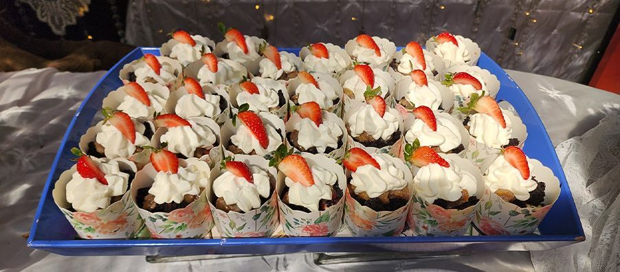 A blue tray filled with cupcakes with whipped cream and strawberries on top.