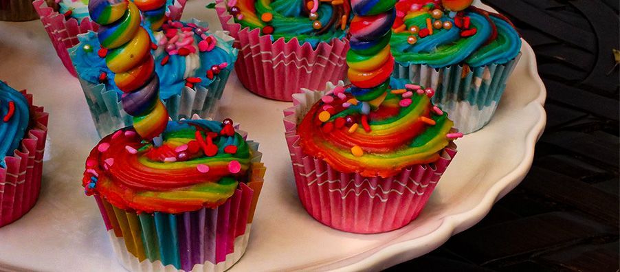 A white plate topped with colorful cupcakes with rainbow frosting and sprinkles.