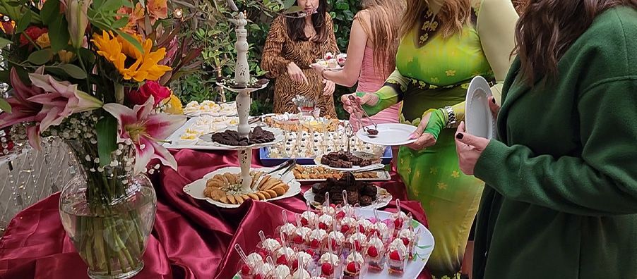 A group of people are standing around a table filled with food.