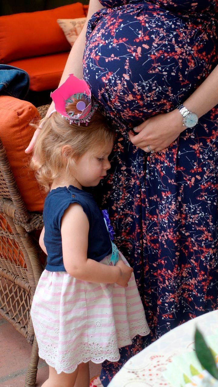 A little girl is standing next to a pregnant woman.