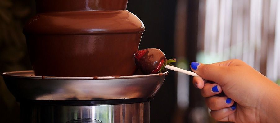 A person is dipping a strawberry in a chocolate fountain.