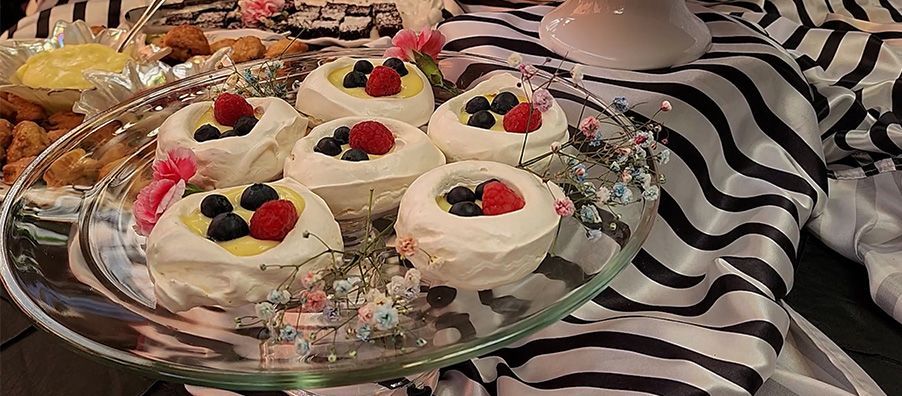 A glass plate topped with cupcakes with raspberries and blueberries on a table.