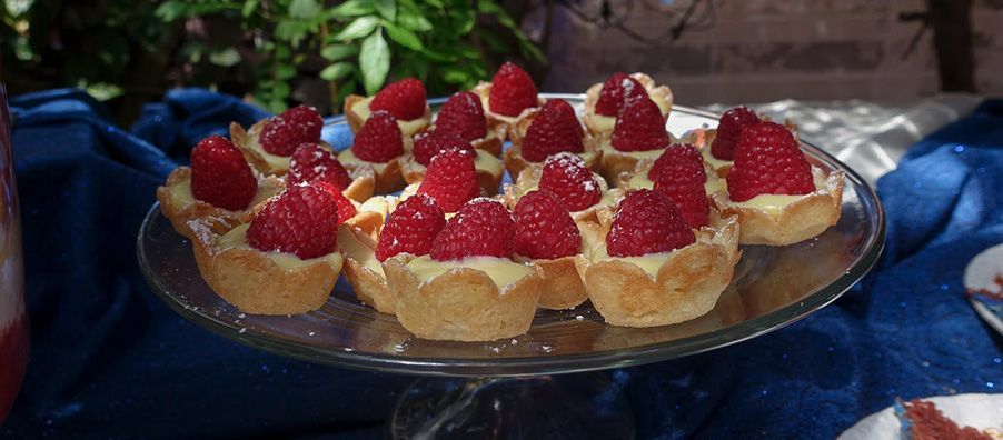 A glass plate topped with raspberry tarts on a table.