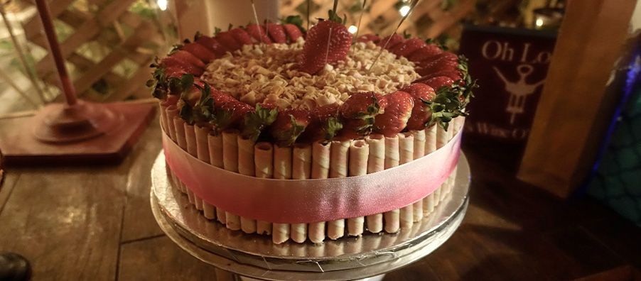 White and strawberry cake with fresh strawberries and strawberry cream-filled pirouline cookies and a ribbon. made by bexx secret garden