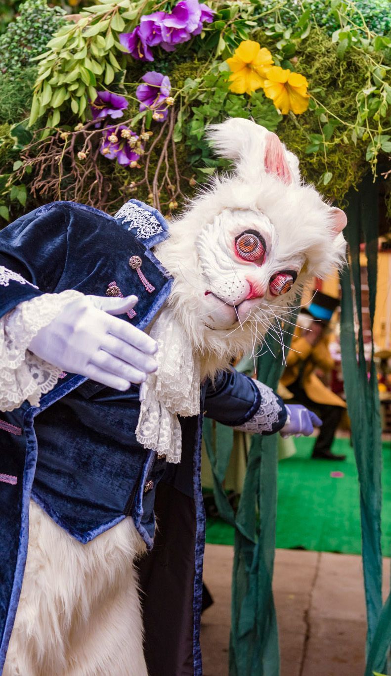 A person in a white rabbit costume is standing in front of flowers.