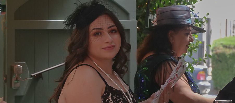 A woman in a black dress and a hat is standing next to another woman.