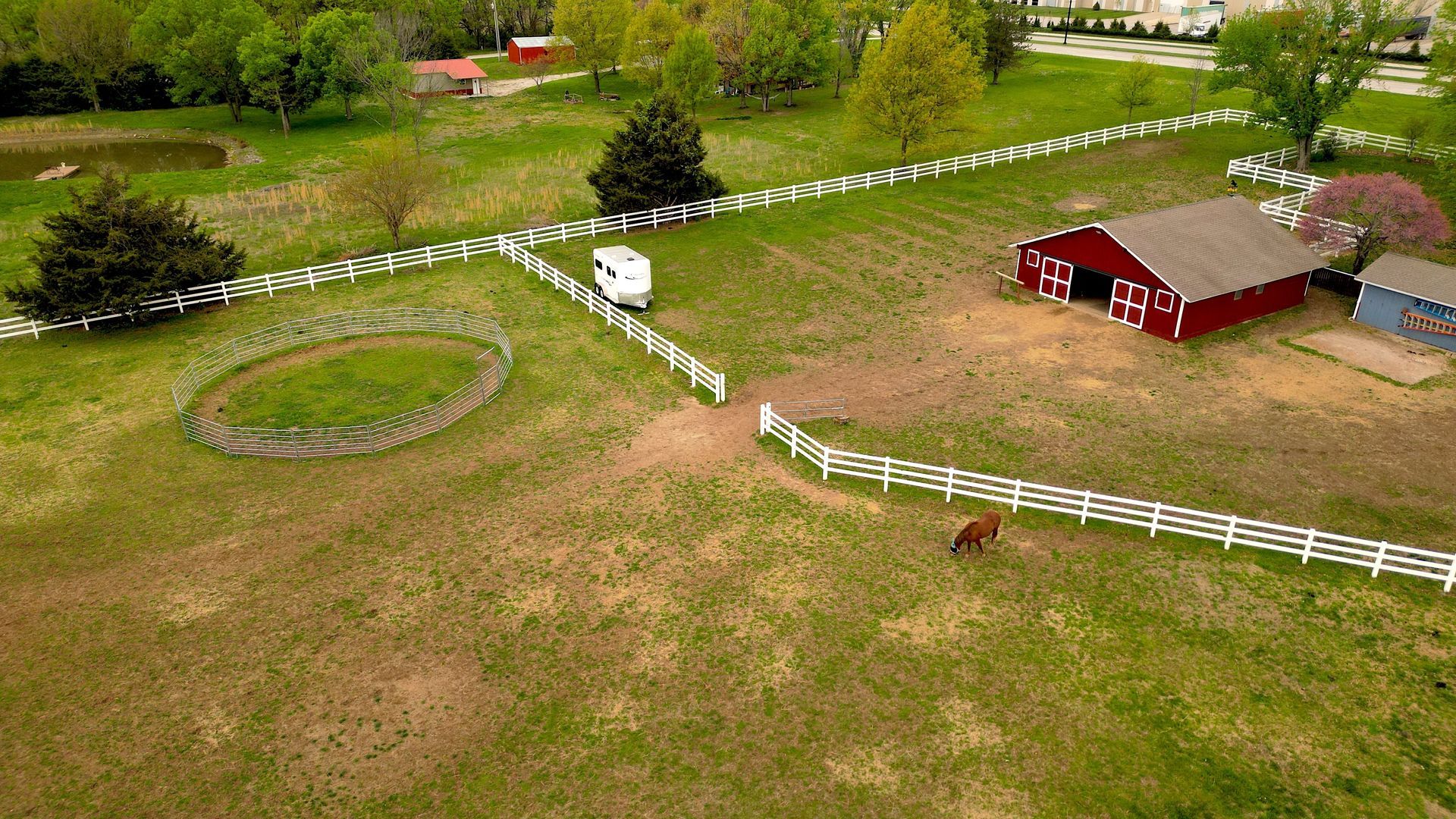 An aerial view of a horse farm with a red barn and a white fence.