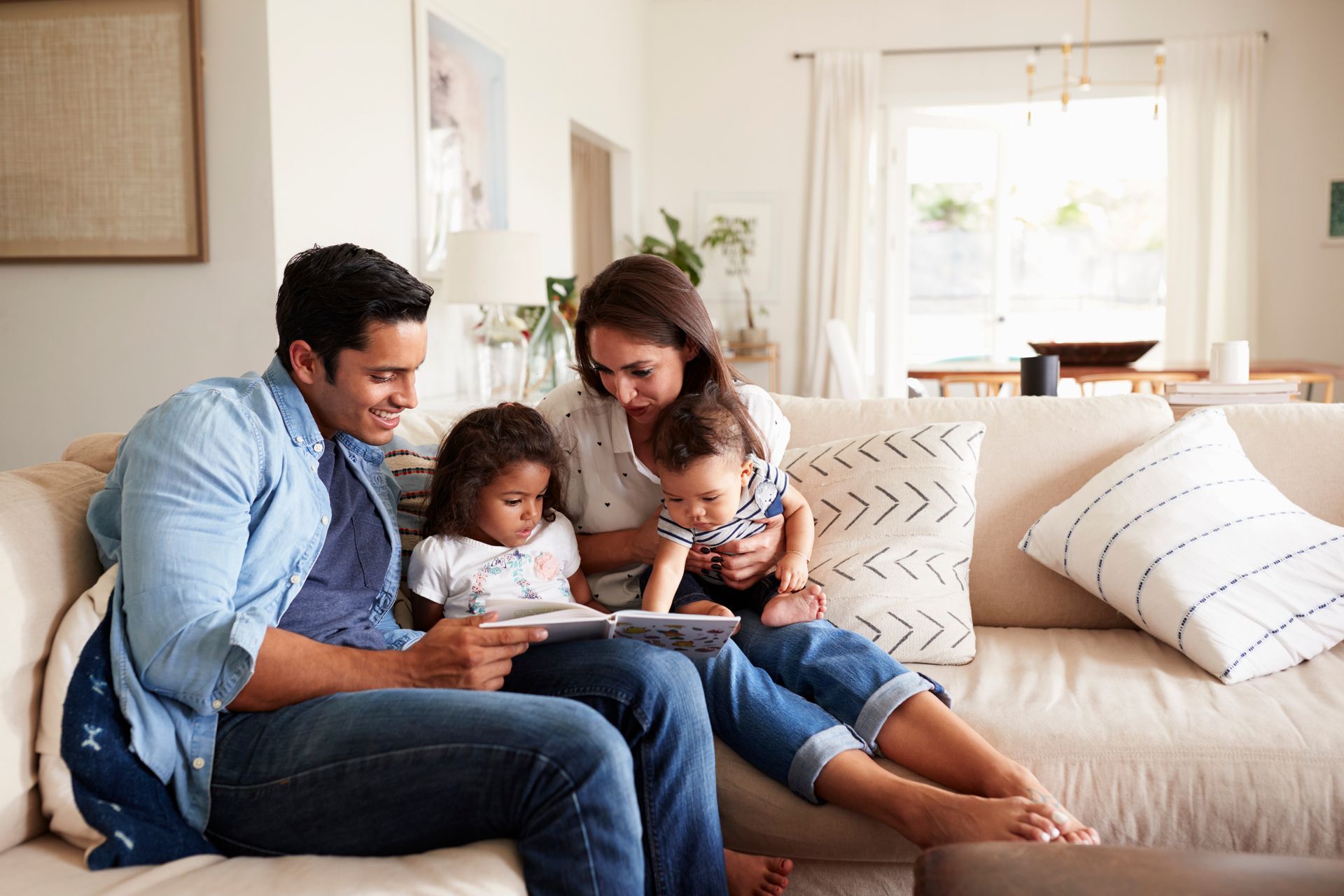 Family sitting on a sofa together, looking at a tablet in a bright living room.