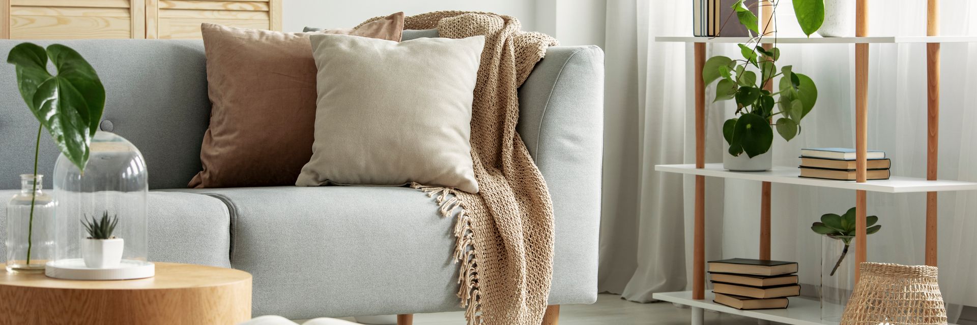 Cozy modern living room with gray sofa, brown pillows, knit throw, plants, and gold shelving.