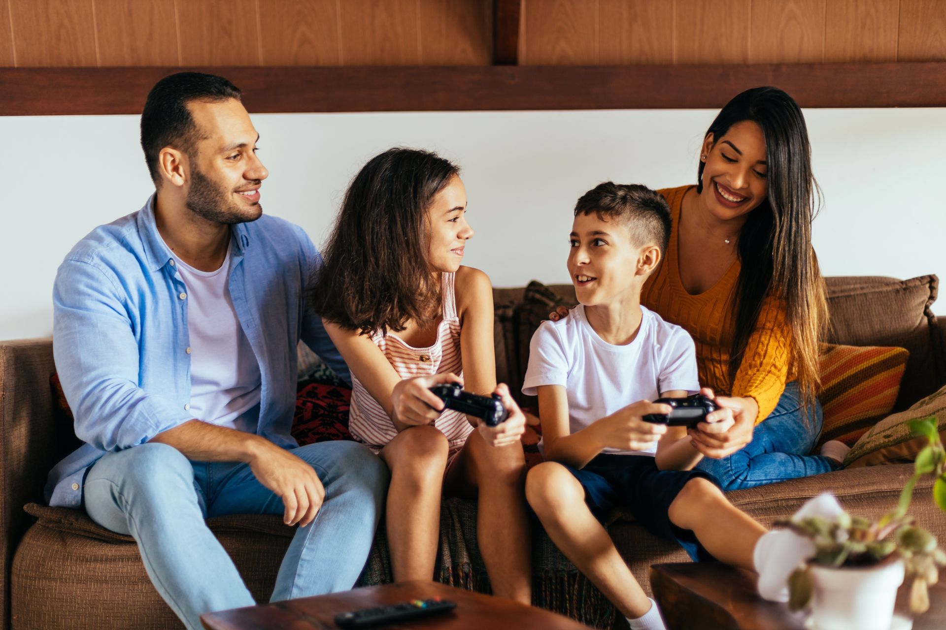 Four people sitting on a couch playing video games and smiling in a cozy living room