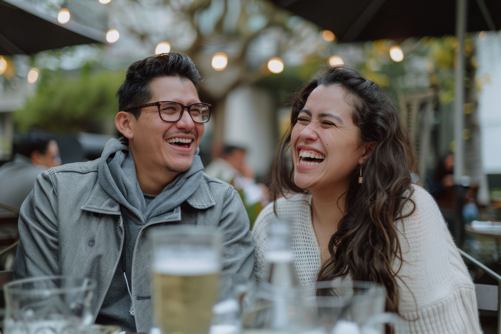 Two friends laughing at an outdoor café with drinks on the table