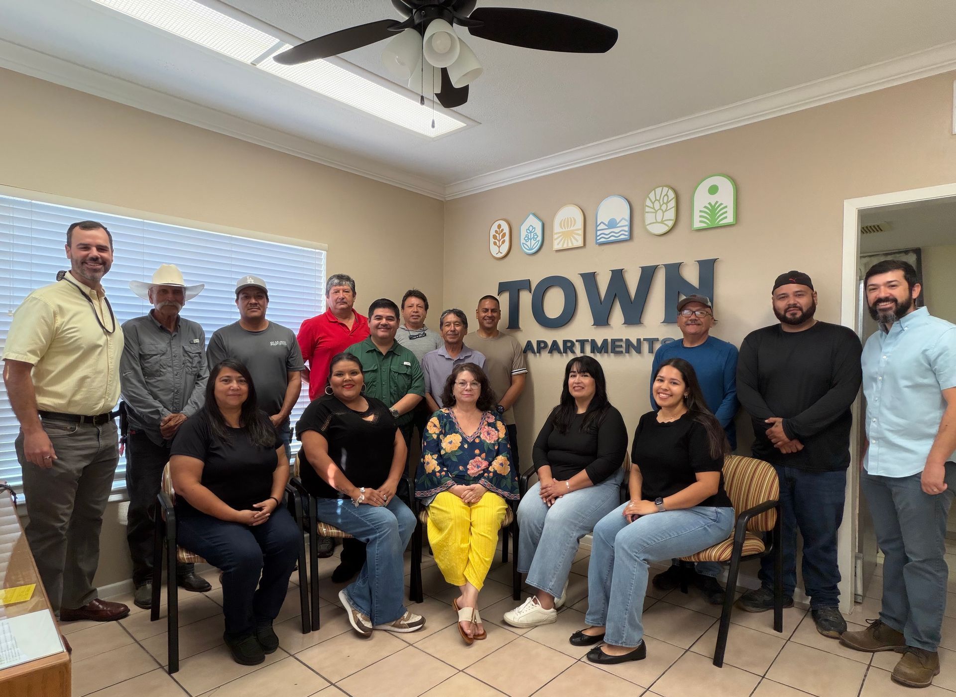Group of people posing in a community room with a “TOWN APARTMENT” sign on the wall.