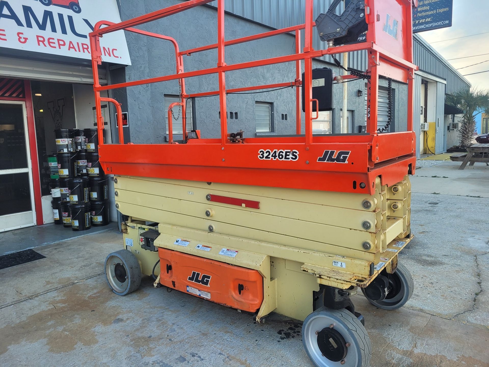 Orange and yellow JLG scissor lift in front of a repair shop.