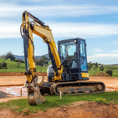 Yellow excavator on dirt and grass, blue sky in background.