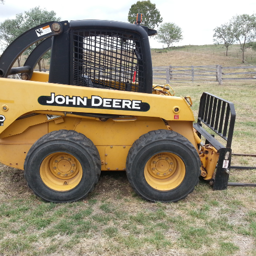 Yellow John Deere skid steer loader with forks on a grassy field.