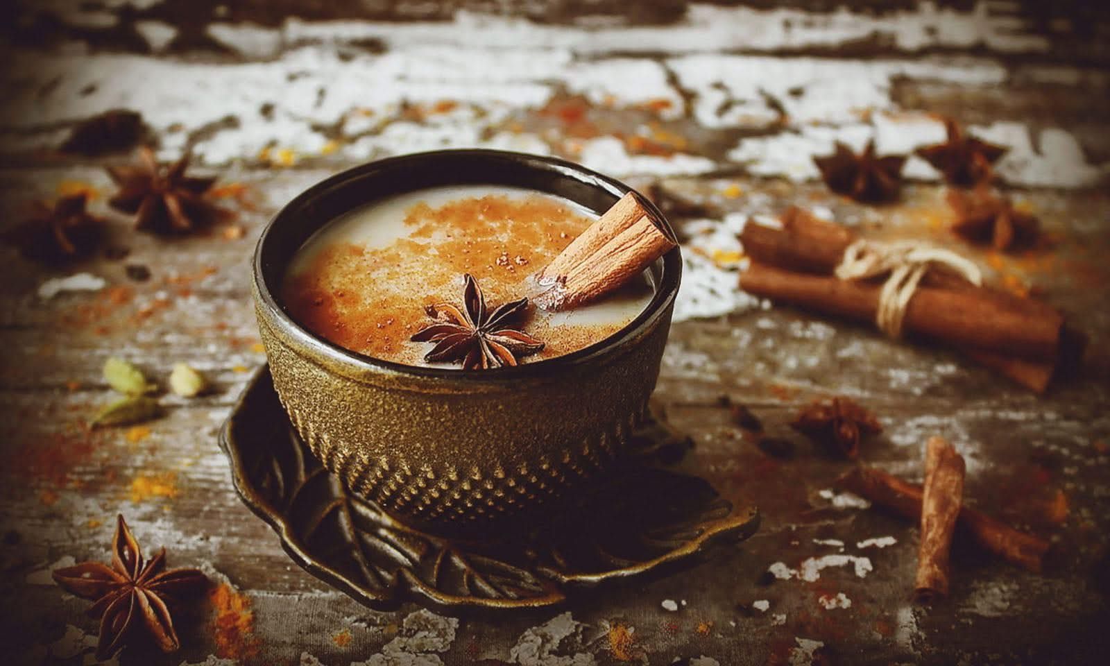 A rustic cup of spiced tea topped with a star anise and cinnamon stick, set on a wooden surface with scattered spices.