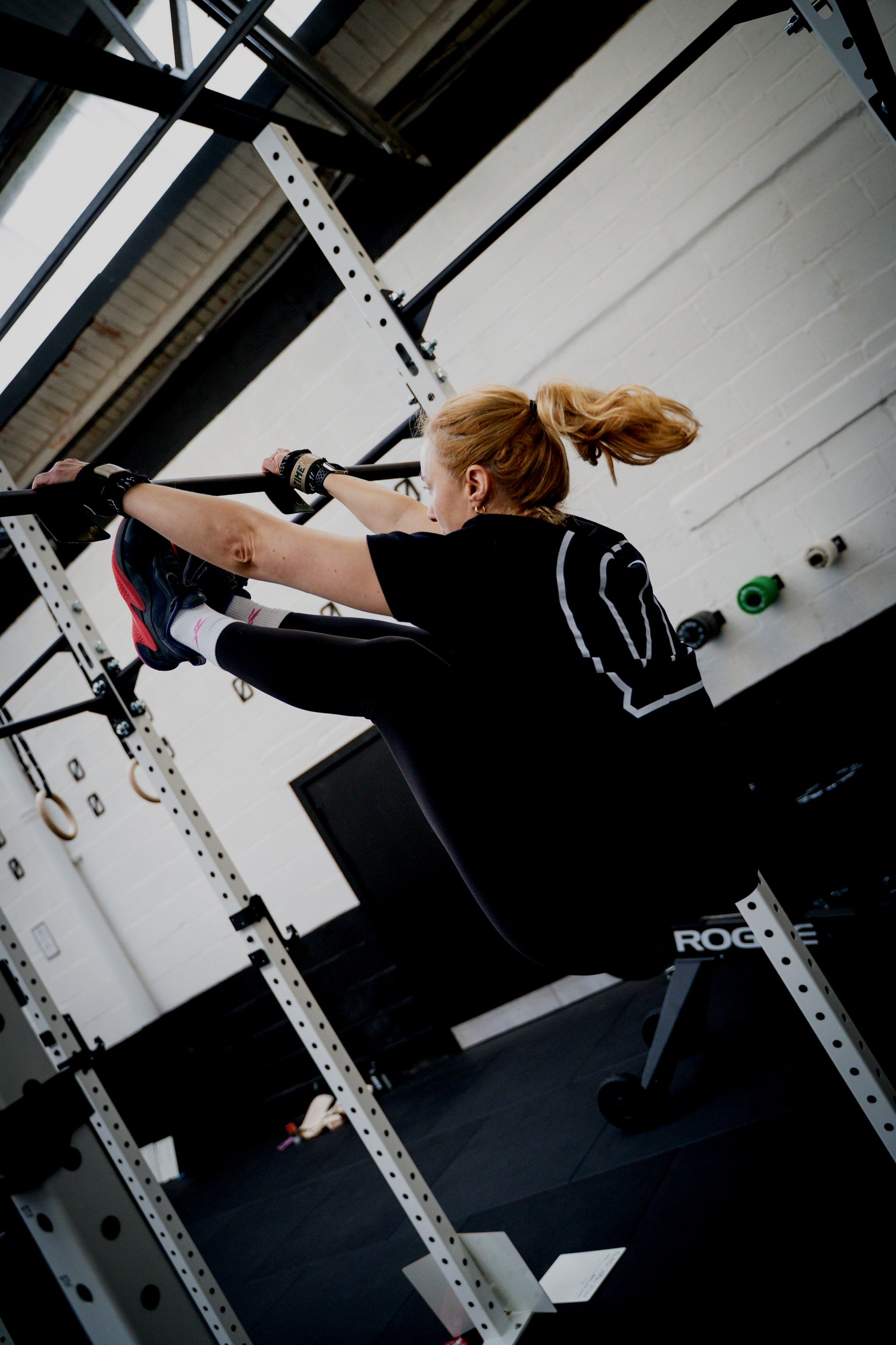 Woman lifting weight overhead in a gym. Black t-shirt, gray leggings. Black weight plate overhead.