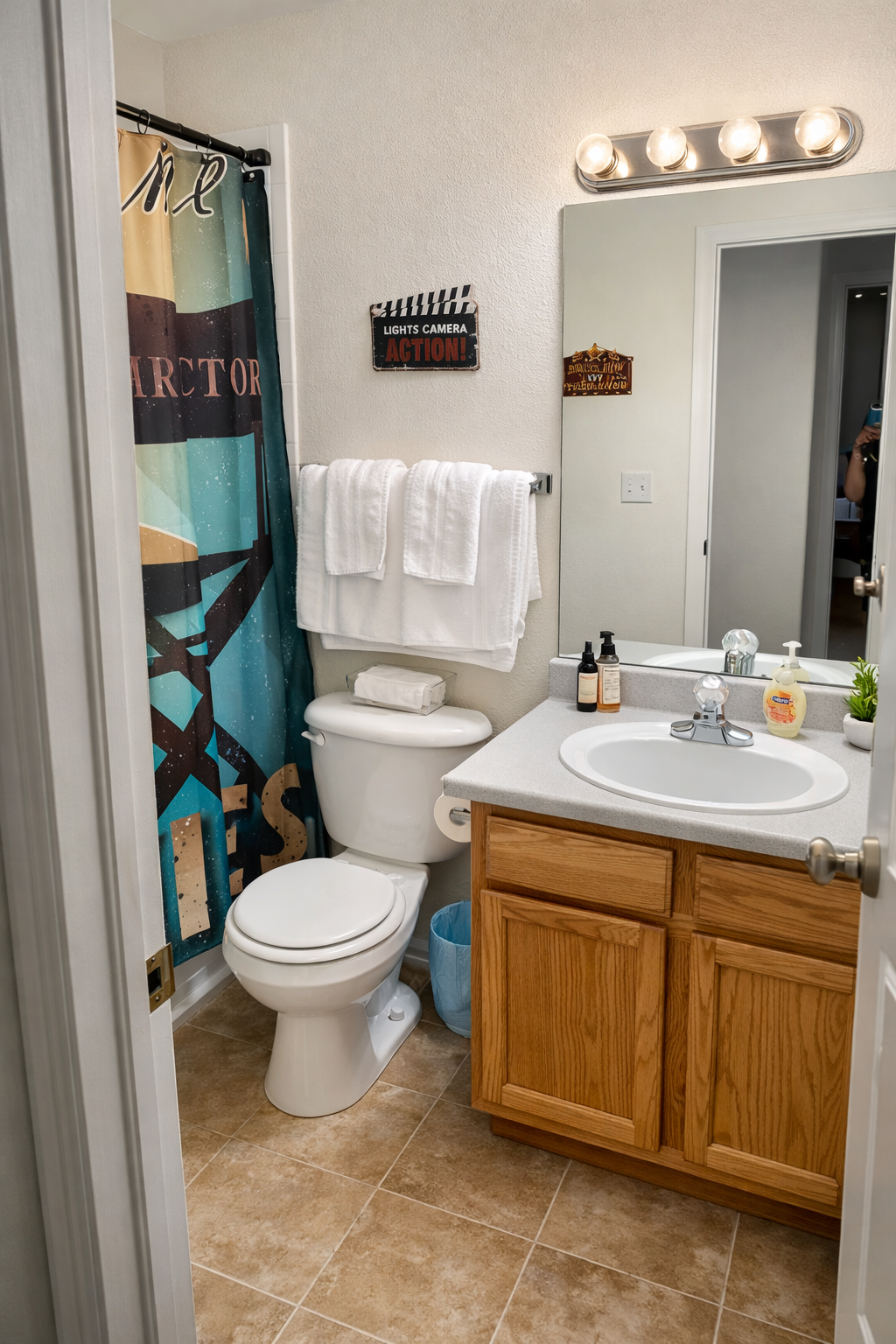Bathroom with toilet, sink, mirror, shower curtain. Tan cabinets, white towels, patterned shower curtain.