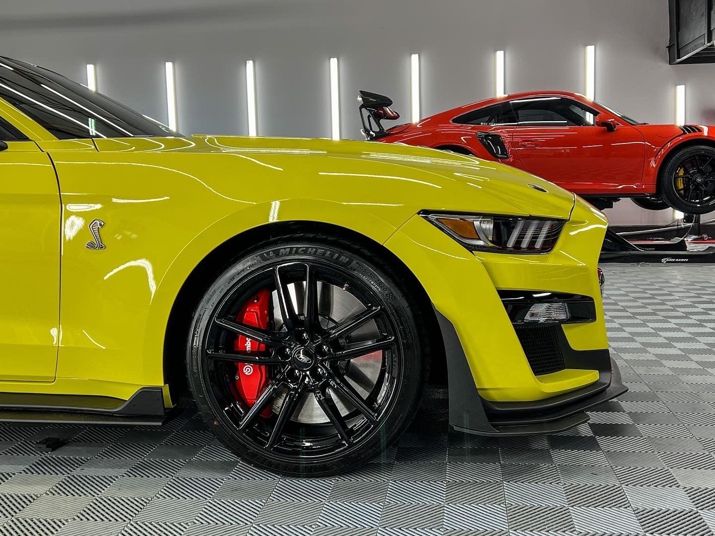 A yellow mustang is parked next to a red mustang in a garage.