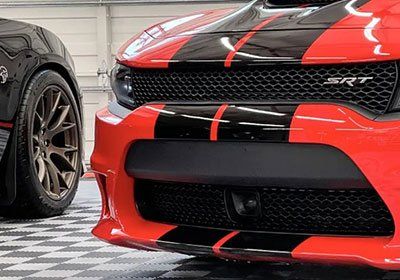 A red dodge charger srt is parked next to a black car in a garage.