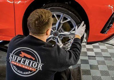 A man wearing a superior auto shield shirt is working on a car wheel.