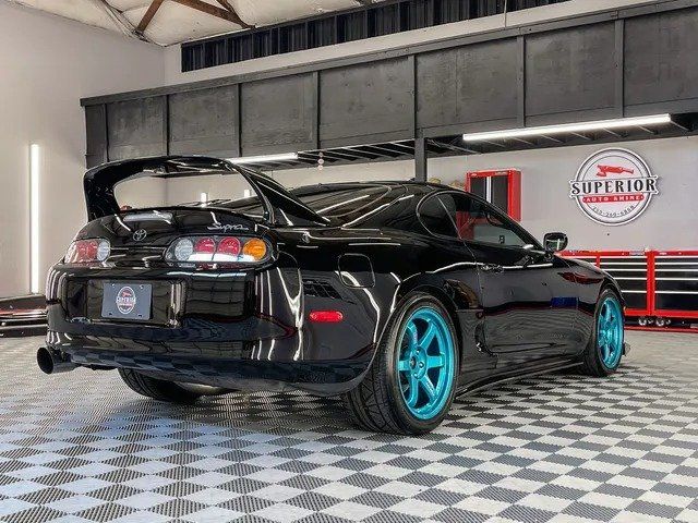 A black car with blue wheels is parked in a garage.