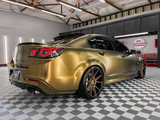 A gold car is parked in a garage on a checkered floor.
