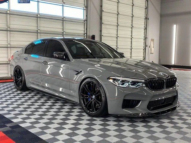 A gray bmw m5 is parked in a garage next to a garage door.