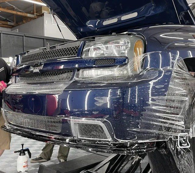 A blue car with the hood up is being wrapped in plastic.