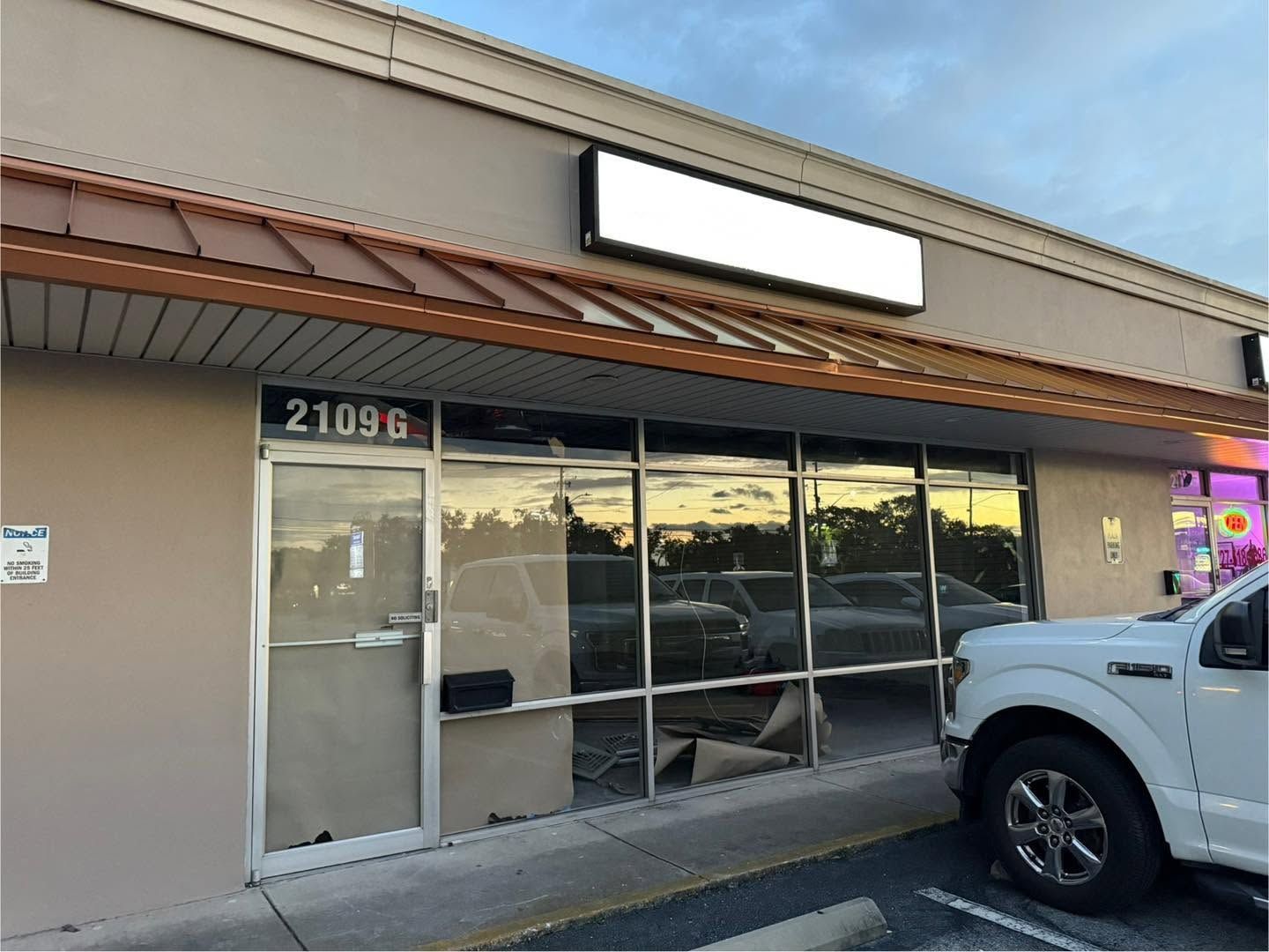 Storefront with blank sign, glass windows, and a white SUV parked in front