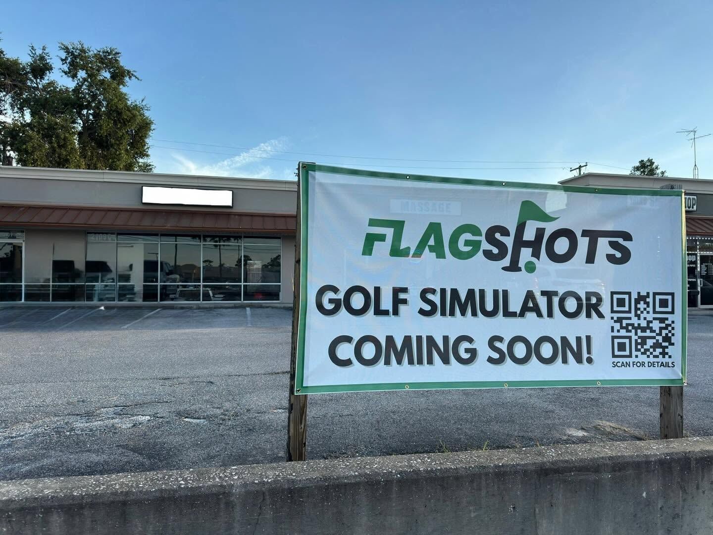 Banner outside a building reads “FLAGS Hots Golf Simulator Coming Soon” on a sunny day.