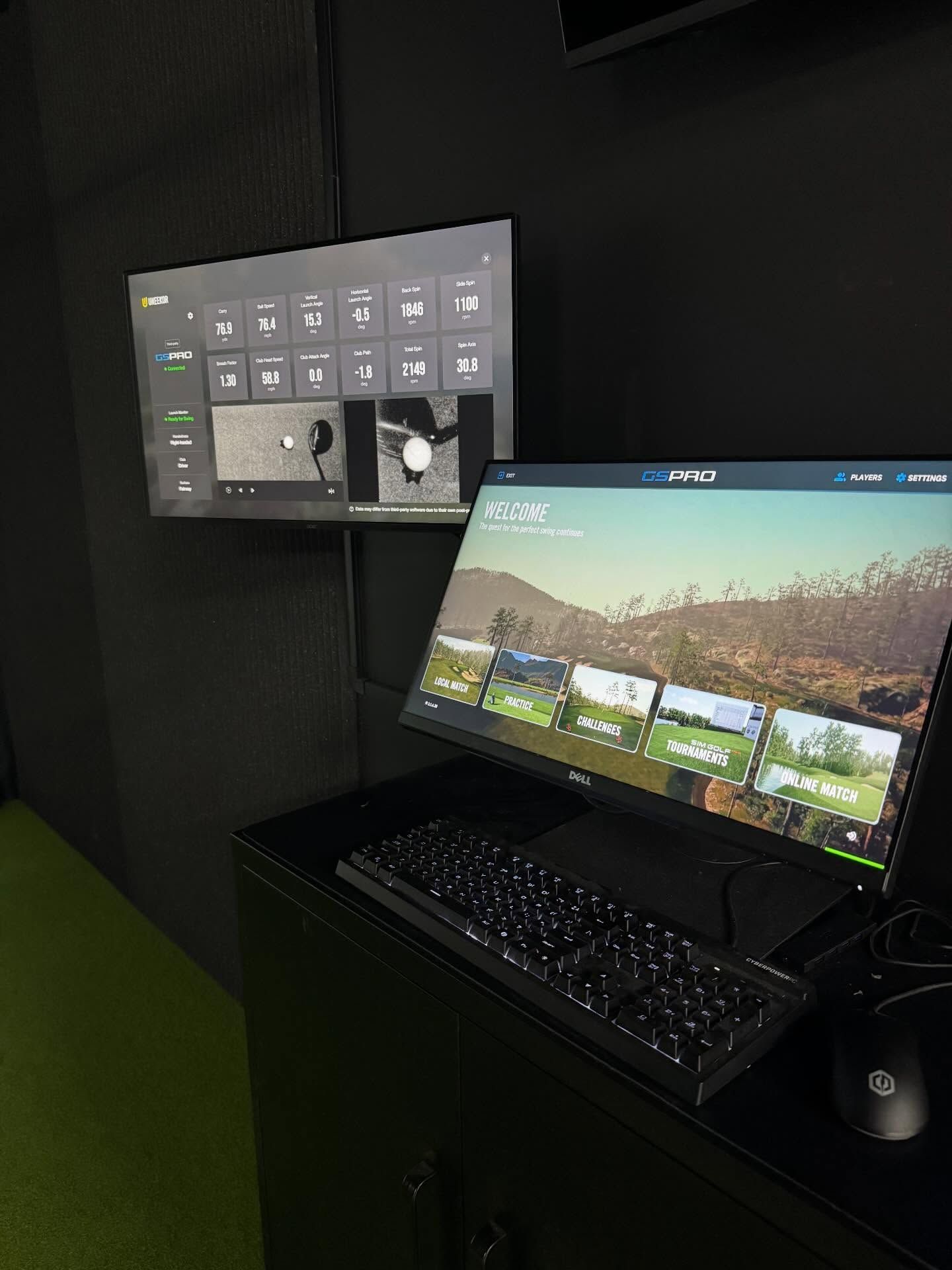 Wall-mounted monitor and desktop PC setup with keyboard and mouse in a dark room.