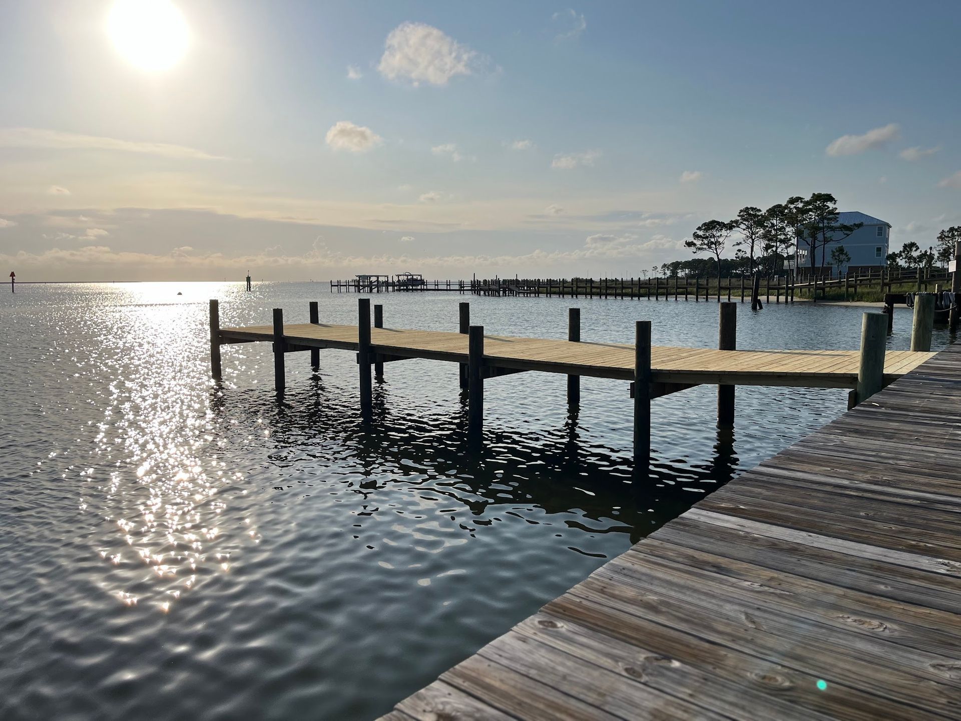 Wooden pier extends over calm water toward a sunny horizon; a building is visible in the distance.