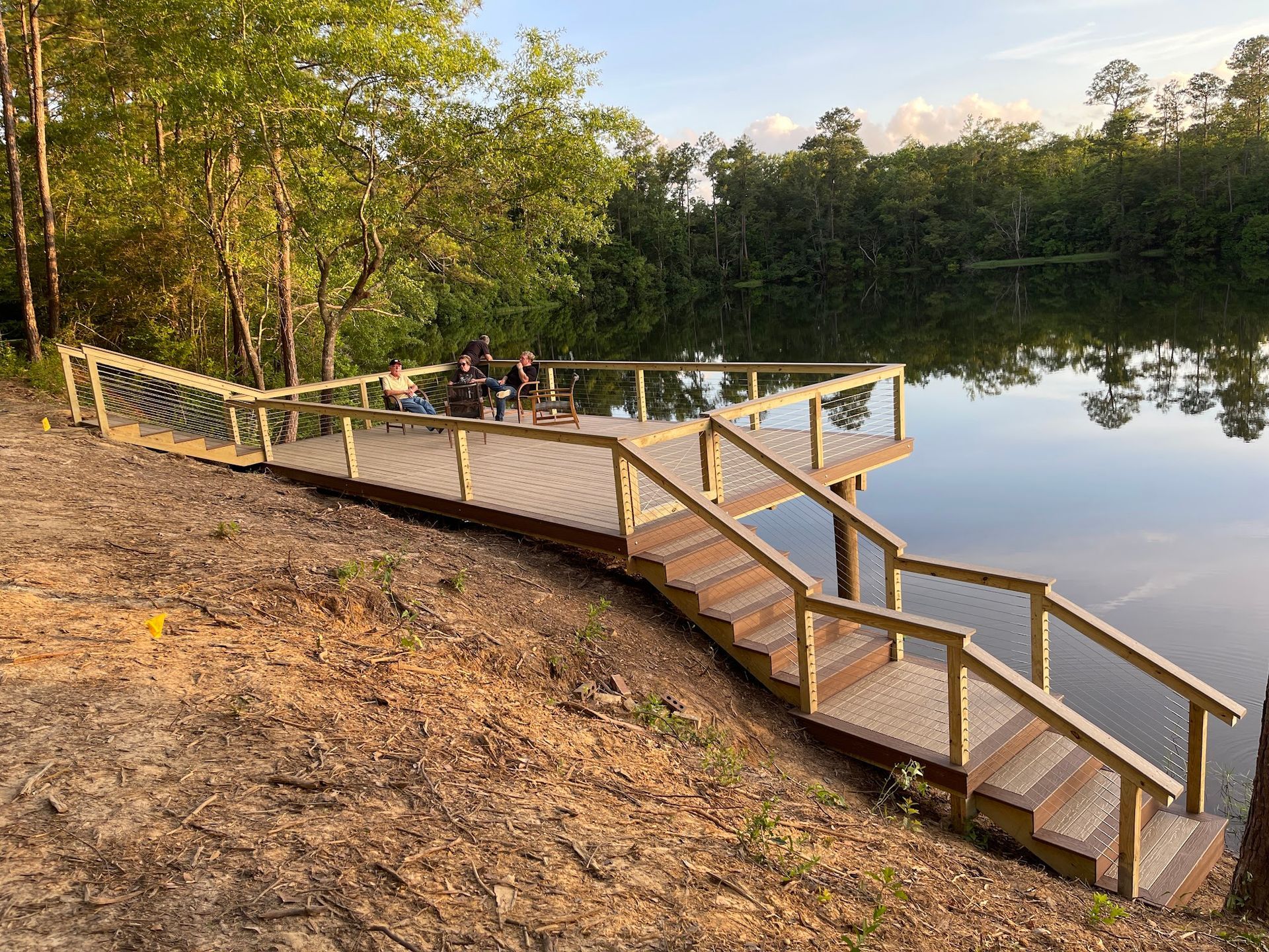 Wooden dock with stairs extending into a calm lake, surrounded by trees.