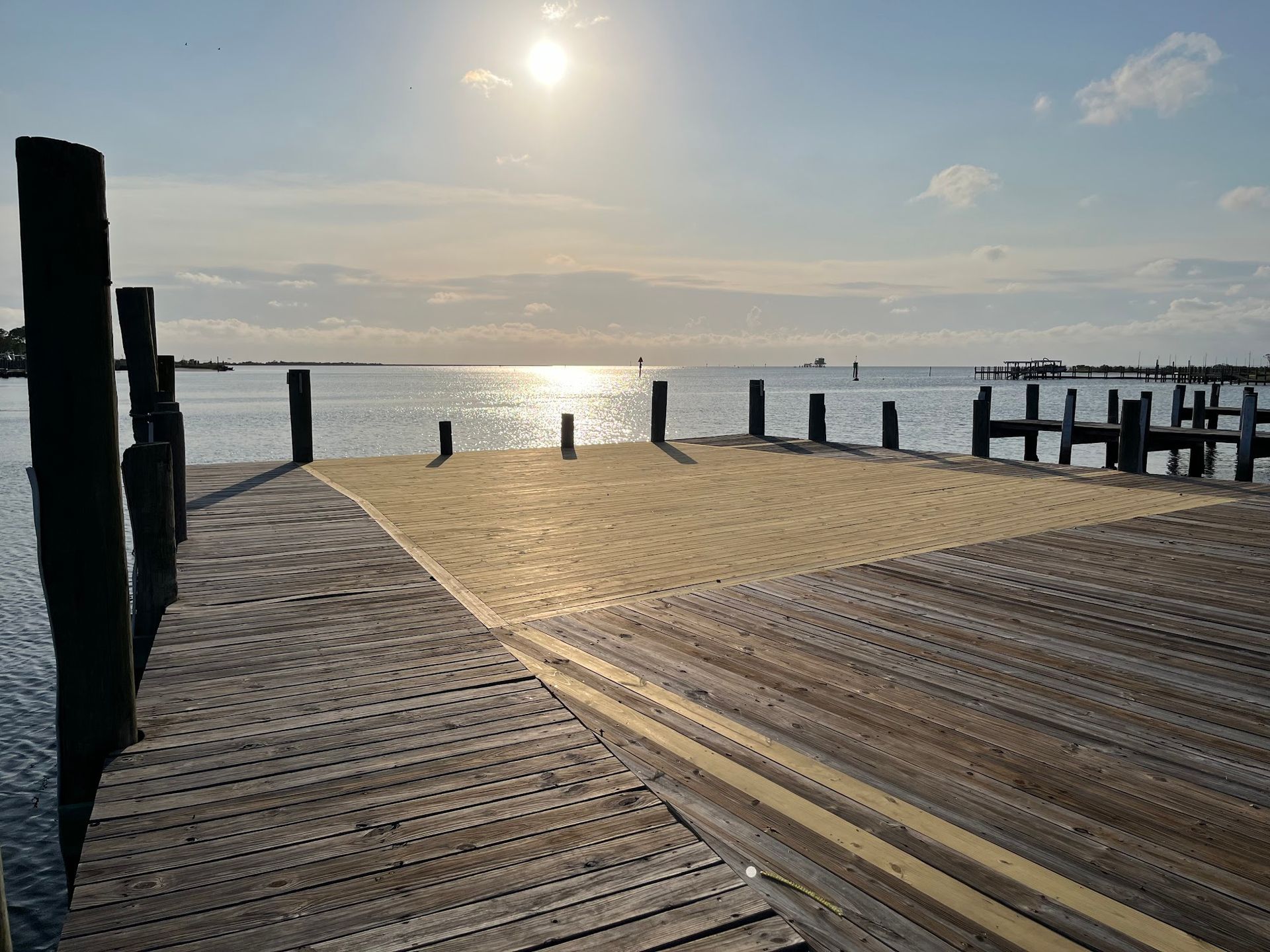 Wooden pier with sand patch, facing a sunny seascape.