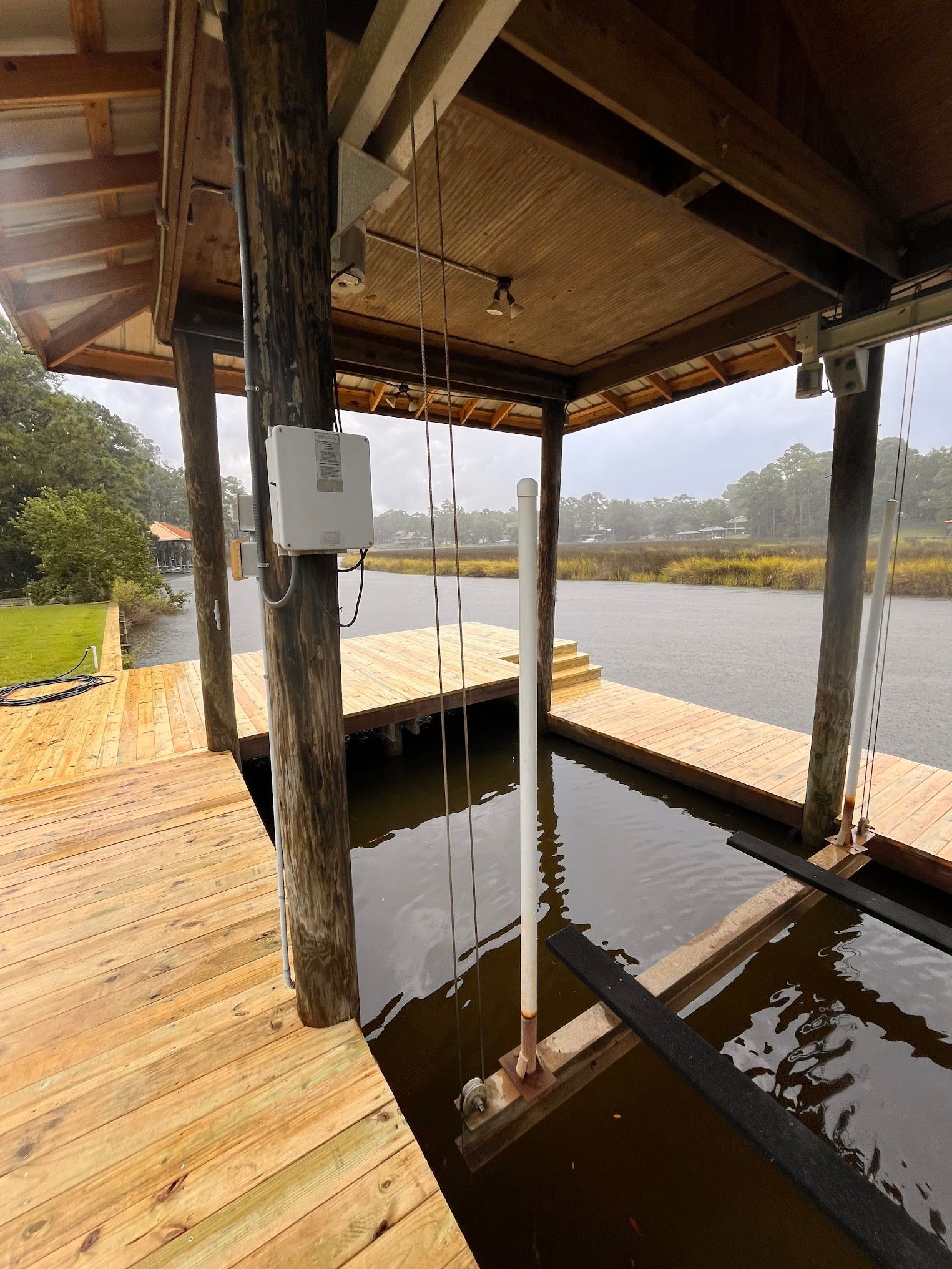 Wooden boat dock with a lift over murky water. Wooden posts support a covered area.