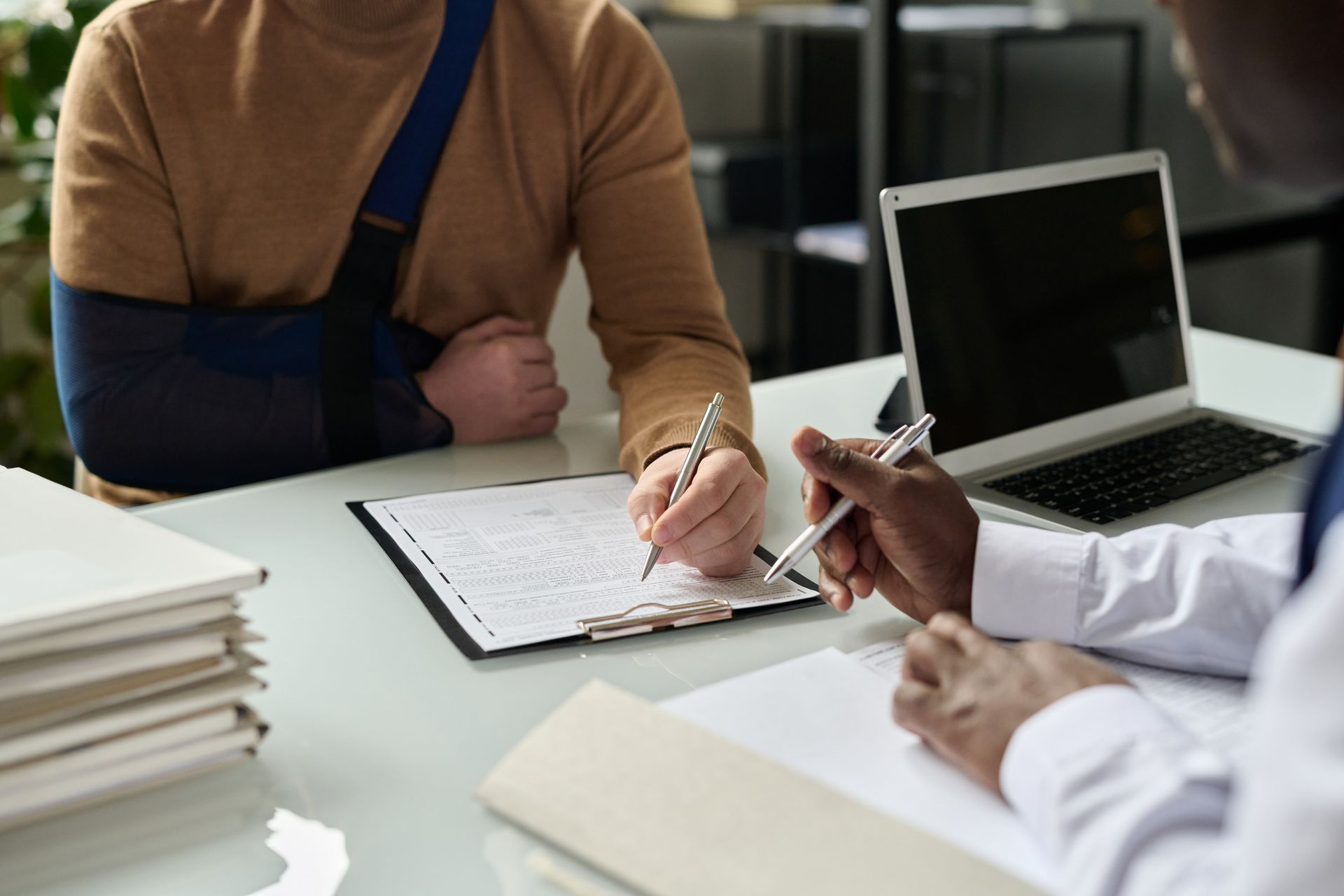 Injured man with arm in sling reviewing legal documents with a motorcycle accident attorney at desk. Injured man with arm in sling reviewing legal documents with a motorcycle accident attorney at desk.
