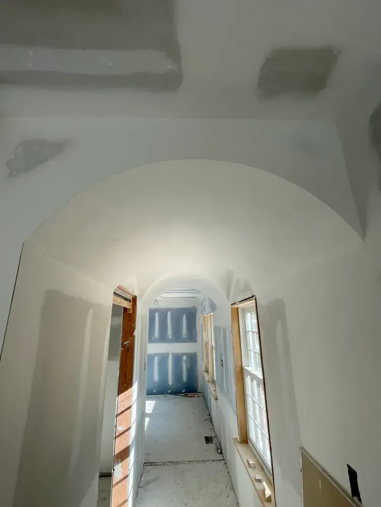 Hallway under construction; arched ceiling, drywall, windows, and sunlight.