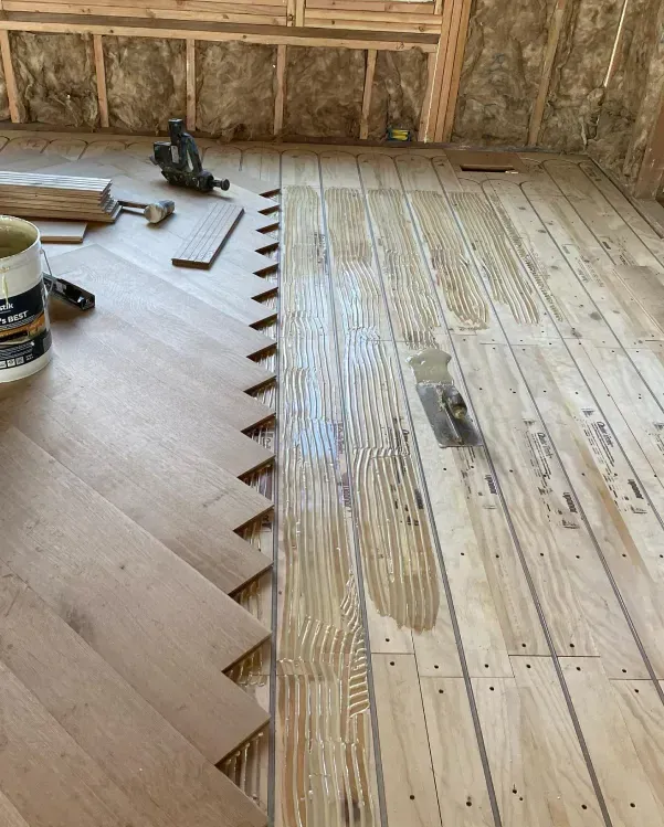 Wood flooring installation in progress; parquet on left, boards on right, adhesive visible.