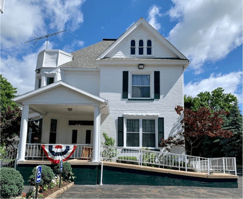 White Victorian house with porch, gabled roof, and red-white-blue bunting under a blue sky.