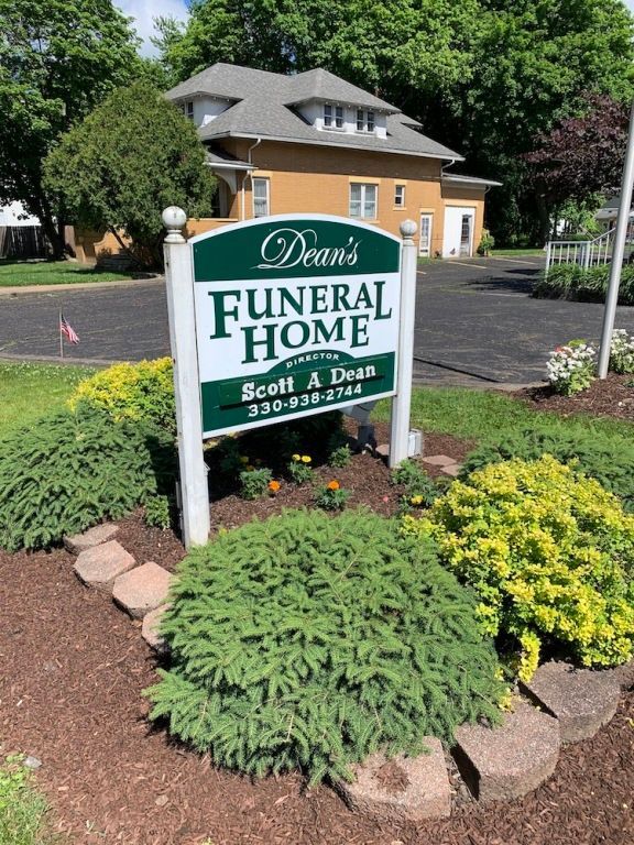 Dean’s Funeral Home sign in front of a brick building with landscaped shrubs and flowers