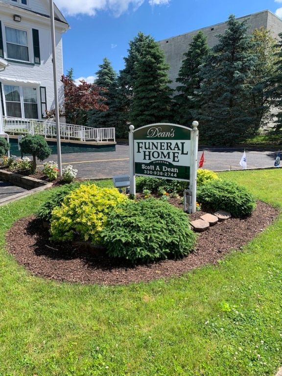Sign for a funeral home in a landscaped front yard with flowers and evergreen trees
